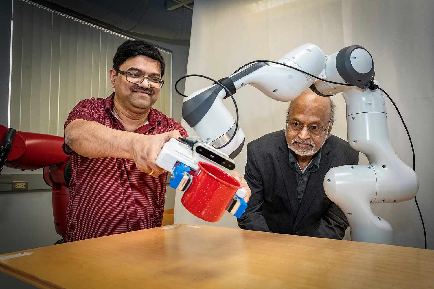 Demonstrating one of the CART designs in a Stony Brook engineering lab are I.V. Ramakrishnan and Nilanjan Chakraborty, who shows how to move the robot’s arm essentially “training” it to hold a cup and move its arm to a designated location. Credit: John Griffin/Stony Brook University