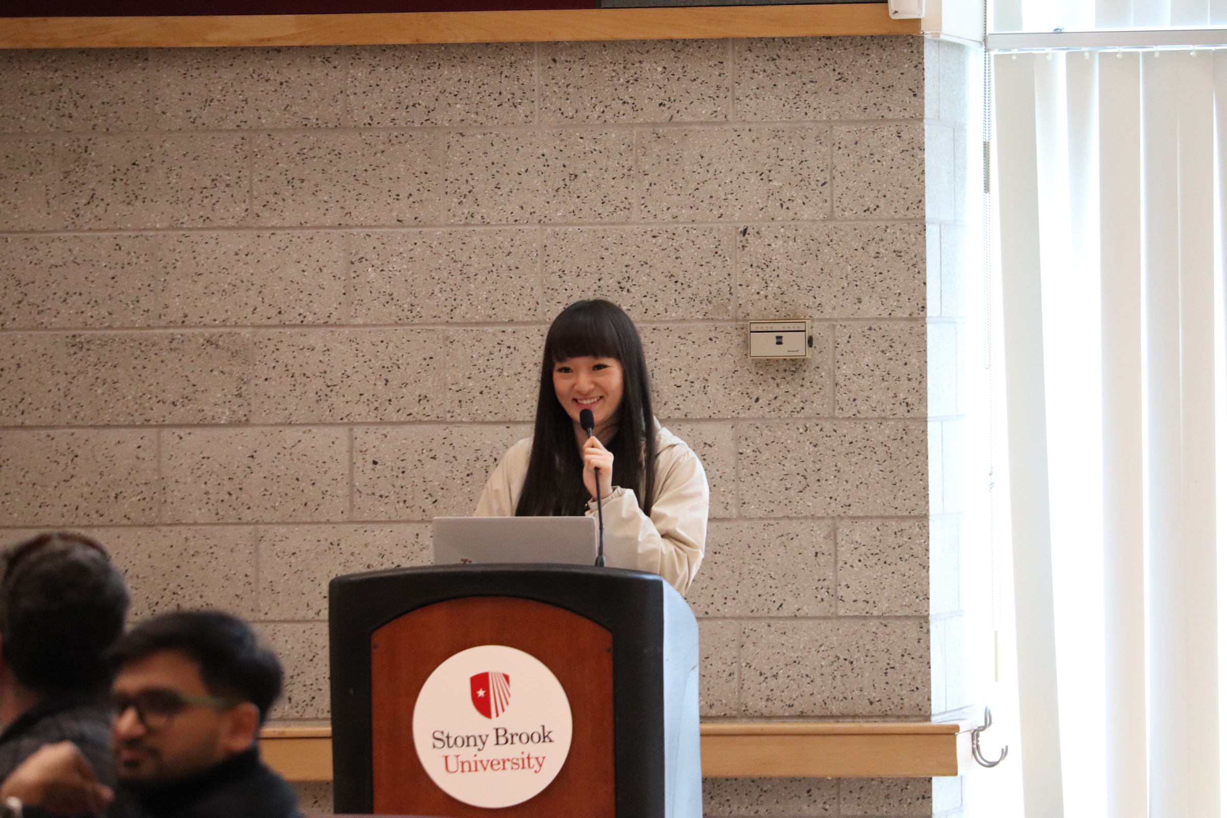 Asian female student with long hair stands behind podium.