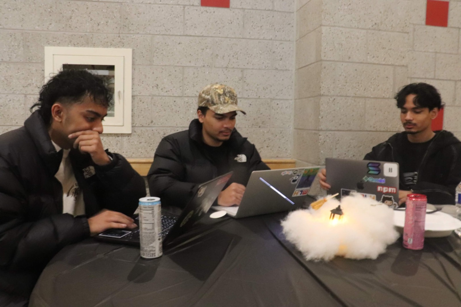 Three young men work on laptops around a table