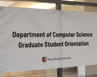A banner with the text "Department of Computer Science Graduate Student Orientation" hangs on the glass doors 