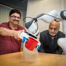 Demonstrating one of the CART designs in a Stony Brook engineering lab are I.V. Ramakrishnan and Nilanjan Chakraborty, who shows how to move the robot’s arm essentially “training” it to hold a cup and move its arm to a designated location. Credit: John Griffin/Stony Brook University