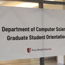 A banner with the text "Department of Computer Science Graduate Student Orientation" hangs on the glass doors 